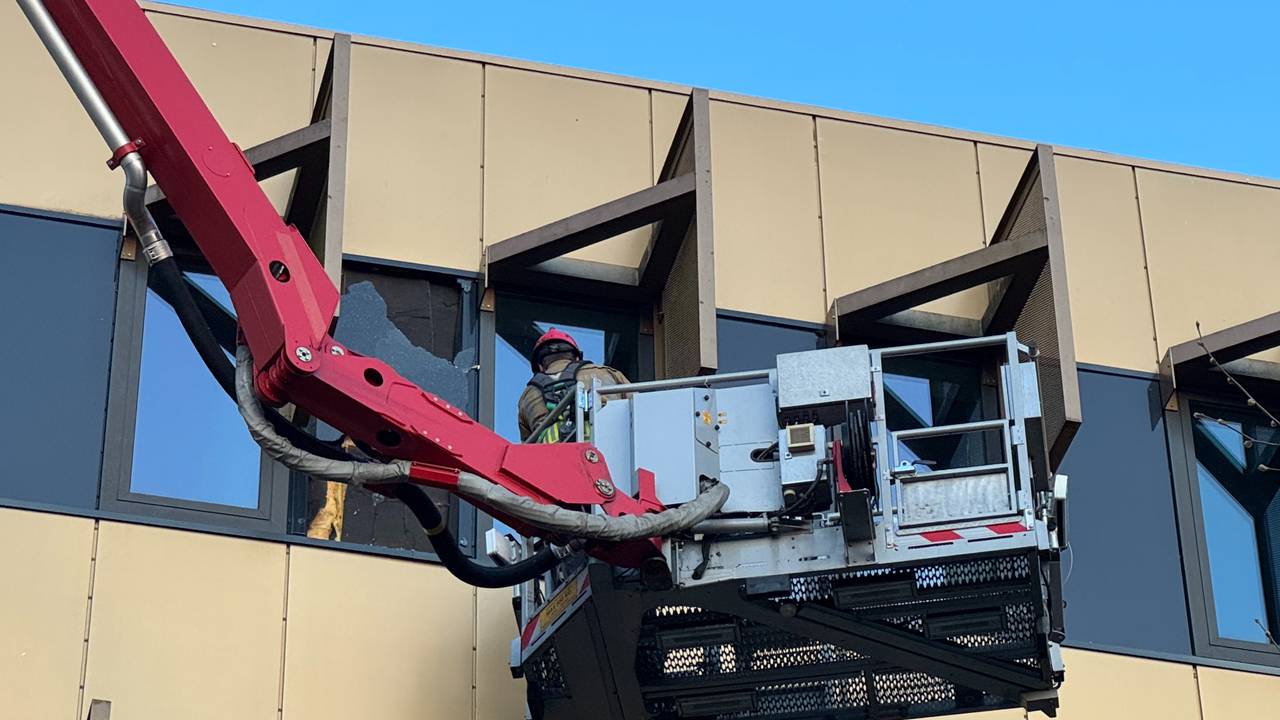 De brandweer haalt de resten van een gesprongen raam weg (foto: Dylan van Mourik).