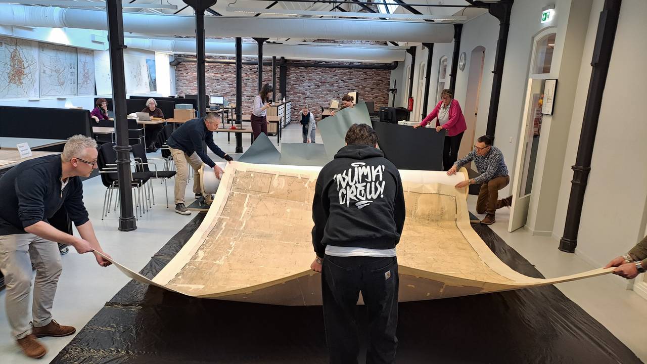 De kaart wordt door maar liefst vijf mensen uitgerold (foto: Regionaal Archief Tilburg).