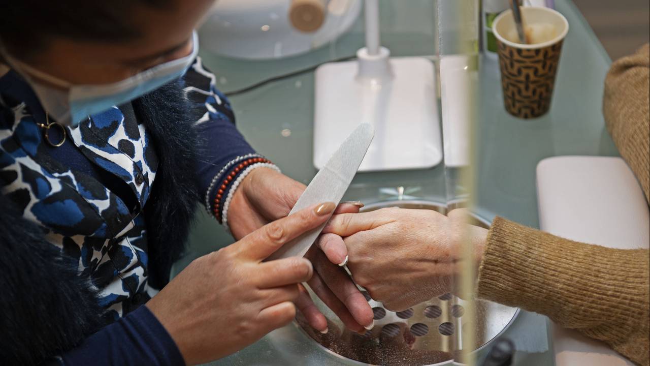 Een nagelstyliste vijlt de nagels van en klant (foto: ANP).