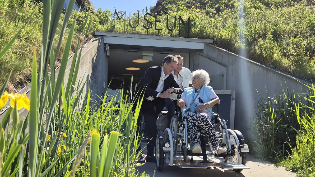 Sjanie Versluis-Ruijtenberg in gesprek met Zonnebloem-ambassadeurs John en Kees de Bever, op de rolstoelfiets van De Zonnebloem bij het Biesbosch MuseumEiland in Werkendam