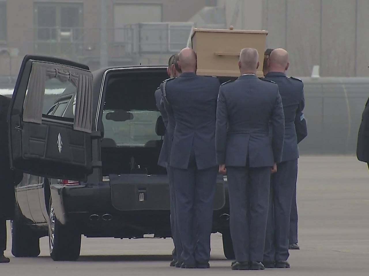 Acht militairen plaatsen kist met stoffelijke resten in lijkwagen.