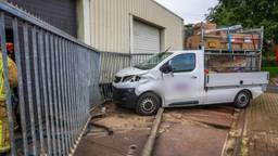 Auto schiet door hek en botst tegen bedrijfspand, bestuurder gewond