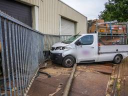 Auto schiet door hek en botst tegen bedrijfspand, bestuurder gewond
