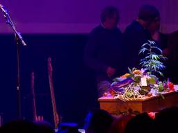 Bloemen en een wietplant op de kist van Armand naast de eenzame microfoon.