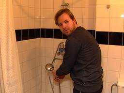 Lars bij zijn douche waaruit alleen koud water komt.