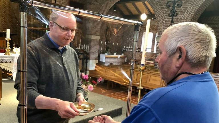 Pastoor Maickel Prasing reikt vanaf zondag de hostie uit met een plastic scherm ertussen (foto: Erik Peeters).