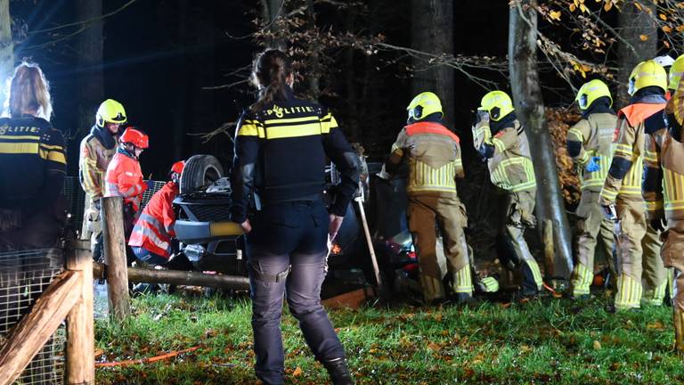 Auto ramt lantaarnpaal en bank en slaat over de kop, bestuurder bekneld