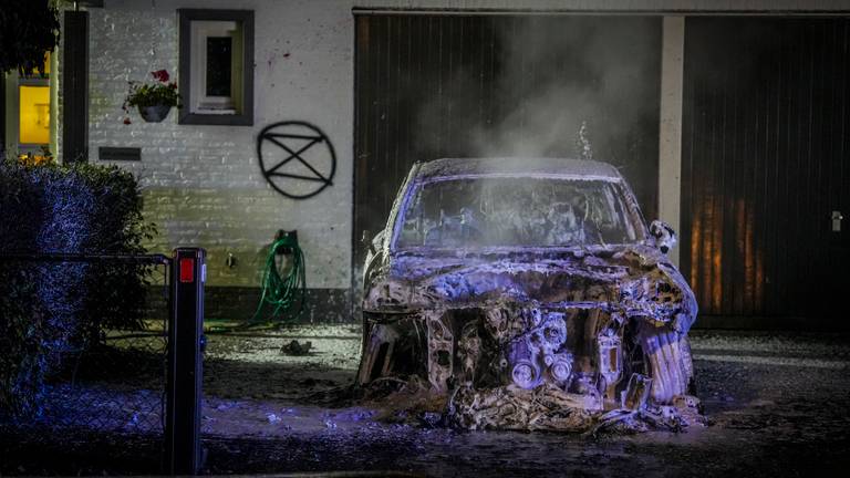 Een van de uitgebrande auto's met op de muur van het huis het teken (foto: SQ Vision).