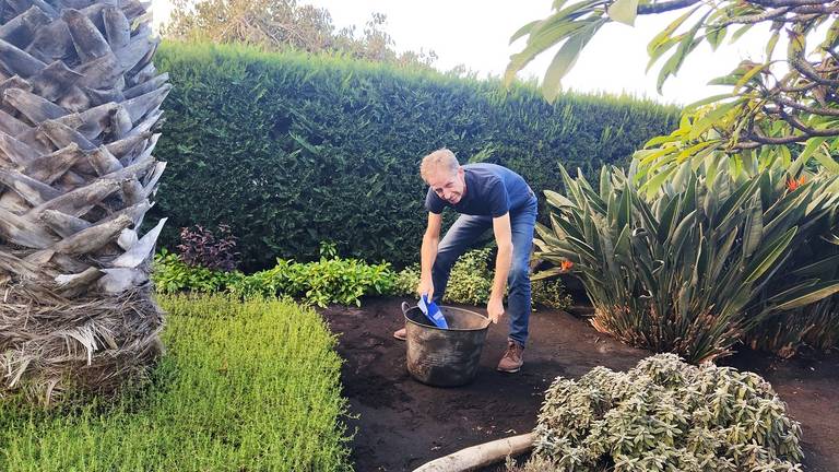 Karel aan het werk: vulkaanas opruimen in de tuin van hun tijdelijke huis. De zon schijnt, maar die zie je niet door de wolken van vulkaanas
