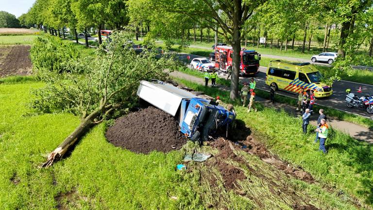 Vrachtwagen rijdt boom uit de grond en kantelt, chauffeur gewond