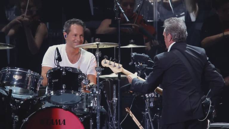 René van Collem tijdens één van de reünieconcerten met Doe Maar, met Henny Vrienten op de rug gezien