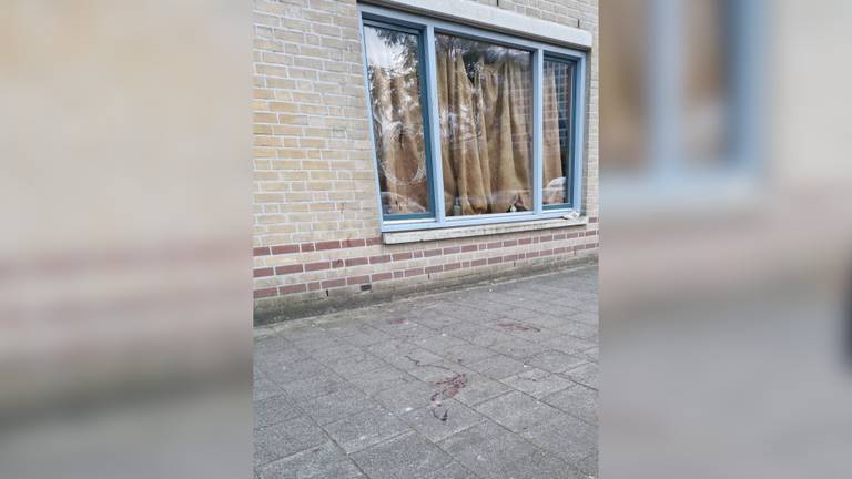 Het raam van de woning is ingeslagen en op straat ligt bloed (Foto: Danique Pals ). 
