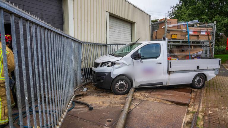 Auto schiet door hek en botst tegen bedrijfspand, bestuurder gewond