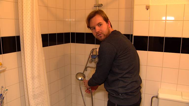 Lars bij zijn douche waaruit alleen koud water komt.