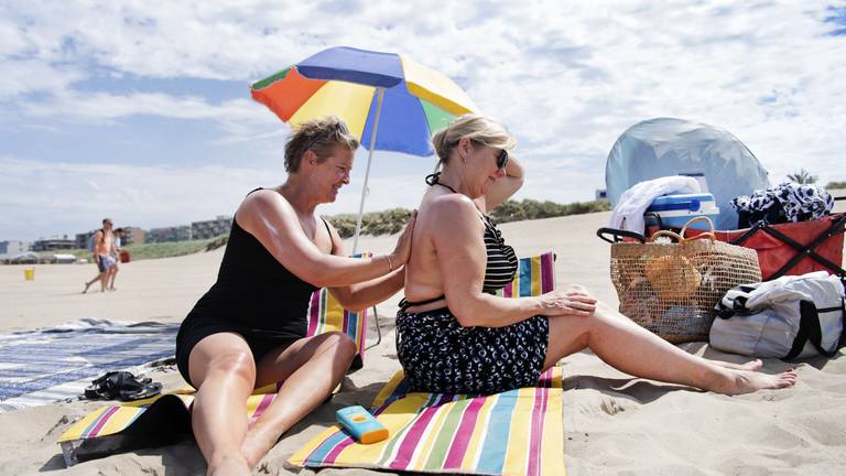 Badgasten op het strand smeren zich in met zonnebrandcrème (foto: ANP).