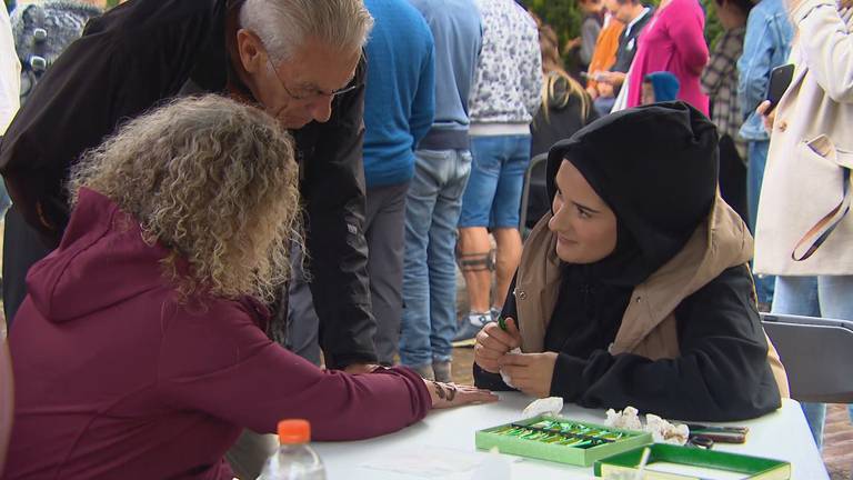 Een bewoonster van het azc praat met bezoekers van de open dag terwijl ze henna zet (foto: Omroep Brabant).