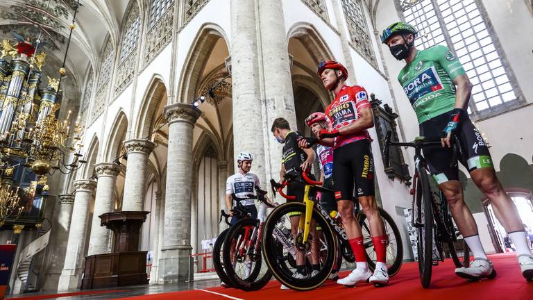 Mike Teunissen in de rode leiderstrui stapt van zijn fiets om samen met Julius van den Berg in de bollentrui een kaarsje aan te steken in de Grote Kerk (foto: Vincent Jannink/ANP).