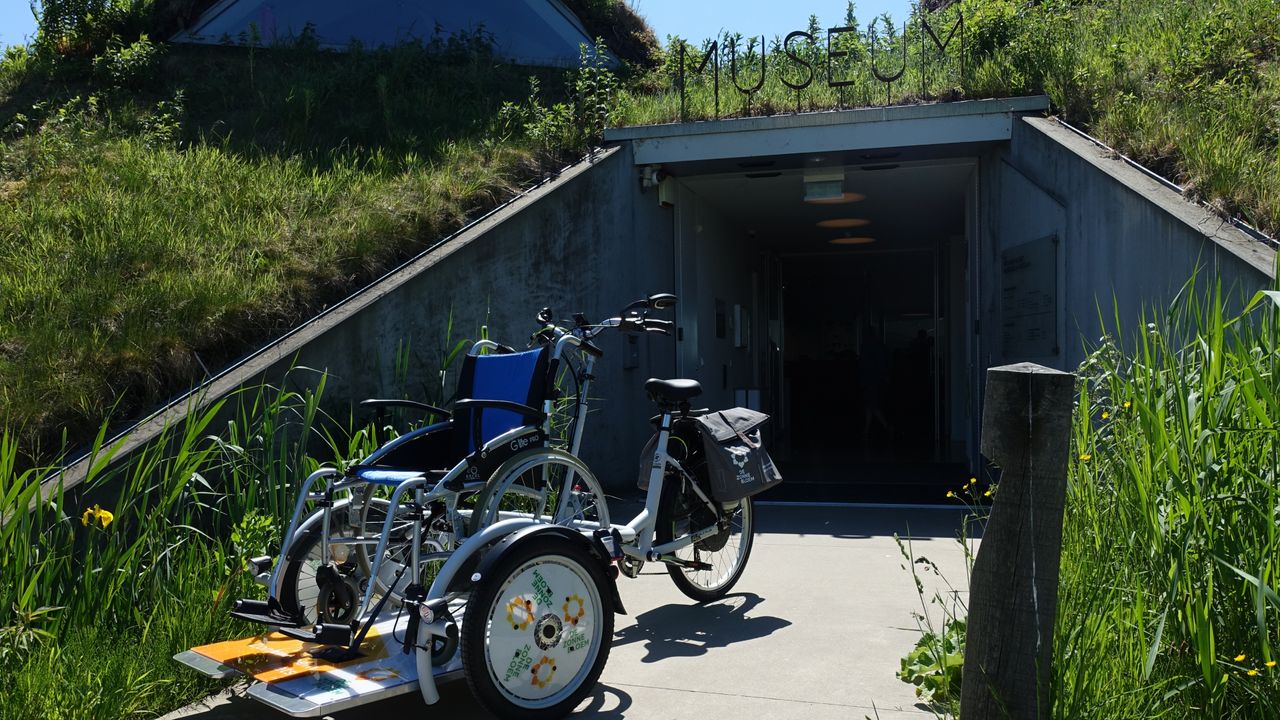 De rolstoelfiets van de Zonnebloem voor de entree van het Biesbosch MuseumEiland in Werkendam (foto: Biesbosch MuseumEiland)