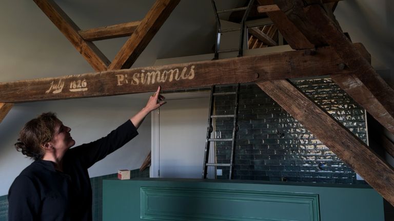 Dieuwke wijst de balk aan met de familienaam van haar man, daarboven het gat dat naar de geheime kamer leidde (foto: Niek de Bruijn)