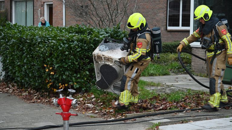 Brandweerlieden tillen de in brand gevlogen wasdroger naar buiten (foto: Toby de Kort/SQ Vision).