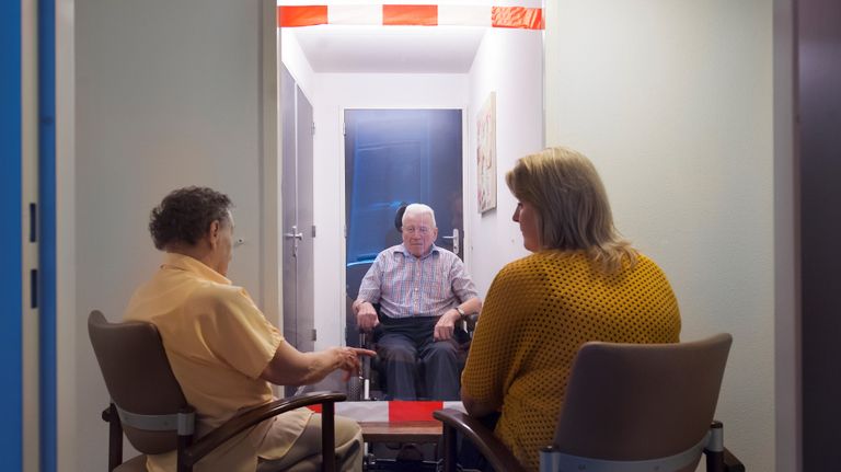 Bezoek wordt in het verzorgingstehuis achter plastic ontvangen. (foto: Regionaal archief Tilburg/ Maria van der Heyden)