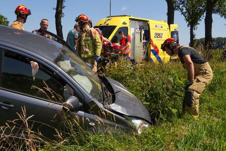 Terwijl ambulancepersoneel zich over het slachtoffer buigt, bekijken brandweerlieden de schade aan de auto (foto: Harrie Grijseels/Persbureau Heitink).