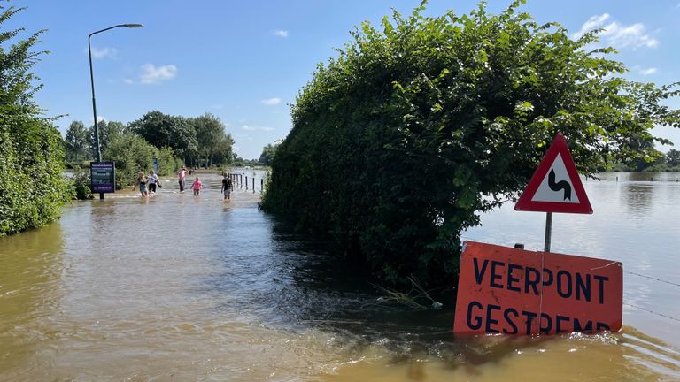Mensen wagen zich in het water van de overstromendeMaas in Sambeek