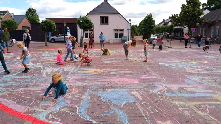 Kinderen druk aan het tekenen op het kerkplein.